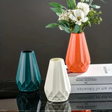 Três vasos geométricos azul-petróleo, branco e laranja, com flores no vaso laranja