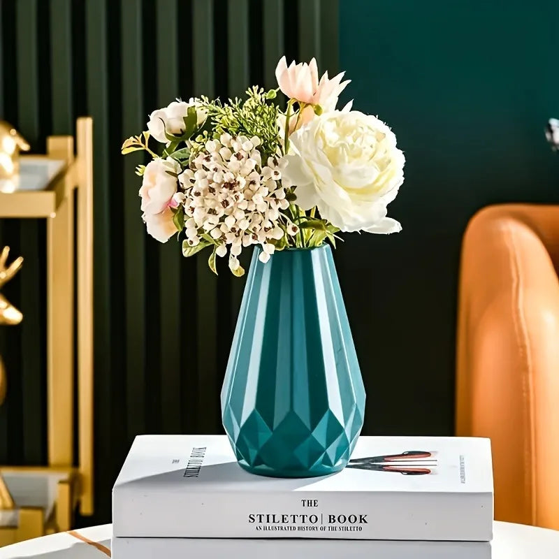 Vaso geométrico azul-petróleo com arranjo de flores claras sobre um livro
