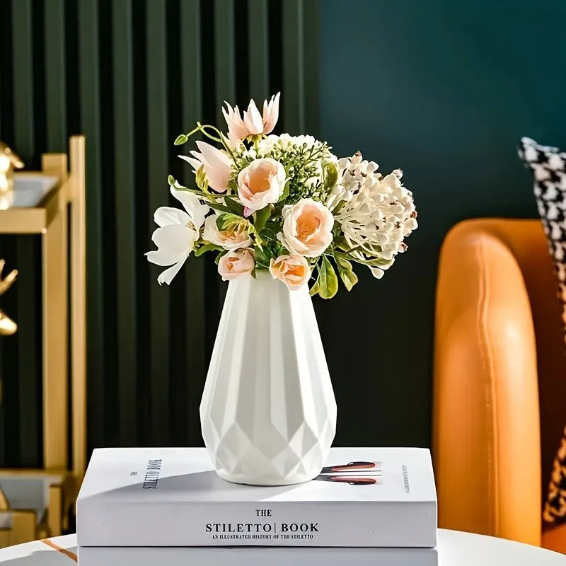 Vaso geométrico branco com arranjo de flores claras sobre livros em uma mesa