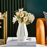 Vaso geométrico branco com arranjo de flores claras sobre livros em uma mesa